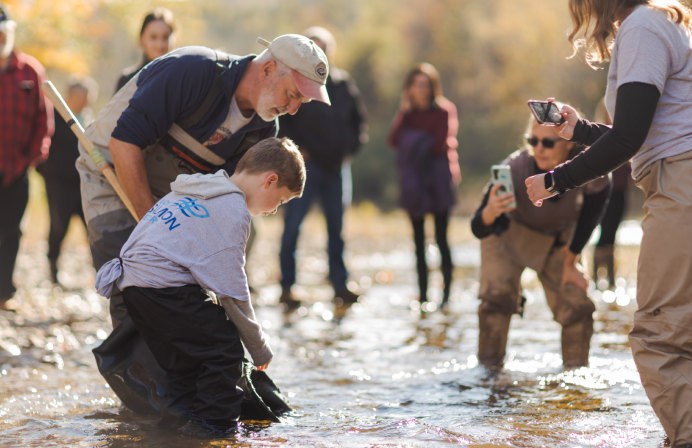 Man and bystanders help child fish with net in river