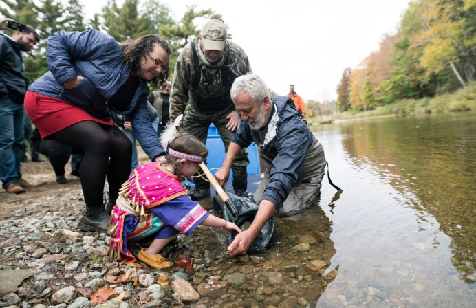 Man and bystanders teach child about salmon